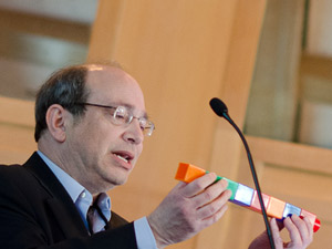 Neil Aronin gebruikt grote Lego blokken om uit te leggen hoe 'gene silencing' medicijnen afgebroken worden tot kleinere moleculen met eigen bijwerkingen. Rechten Foto: Lev Blumenstein, CHDI.